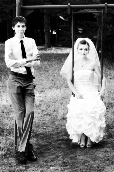 Noiva sentada em baloiços e noivo de pé perto — Fotografia de Stock