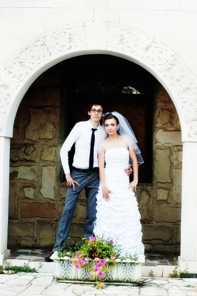 Recién casados se levanta contra una pared de ladrillo en el arco — Foto de Stock