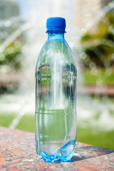Blue bottle with water against blurred fountain — Stock Photo, Image