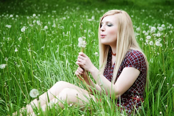 Dziewczyna dmuchanie na mniszek w trawie — Zdjęcie stockowe