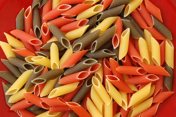 Penne tricolore pasta on red background — Stock Photo, Image