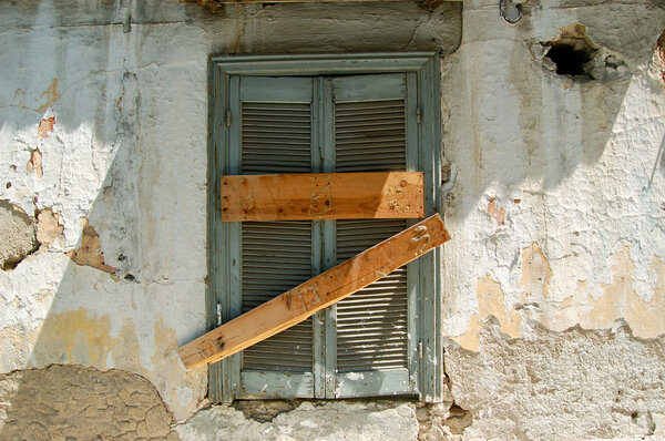 Boarded up old window with blue shutter and peeling paint weathered wall. Abandoned house detail.