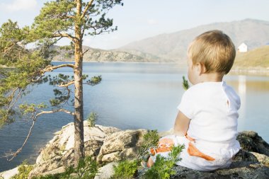 Child seated on the shores of Inlet. clipart