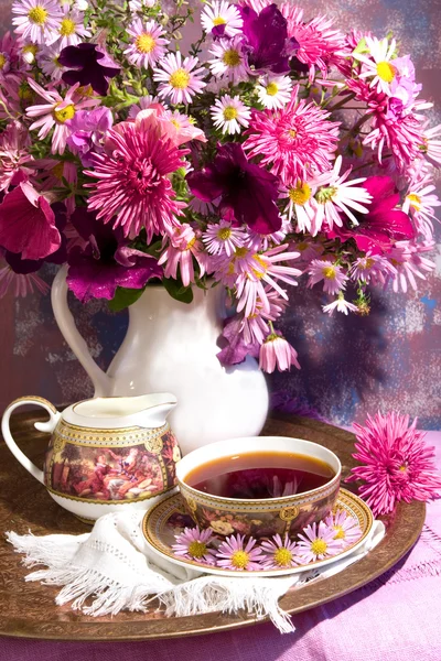 Xícara de chá e um buquê de flores em um jarro branco — Fotografia de Stock