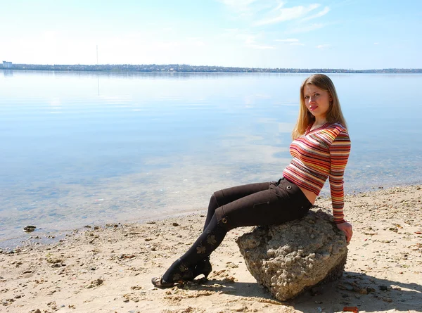 Girl sit at stone on beach of river — Stock Photo, Image