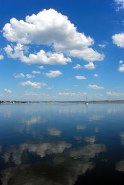 Cloudy blue sky reflection in calm water clipart