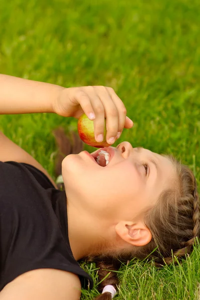 Девочка лежит на лужайке и ест яблоко — стоковое фото