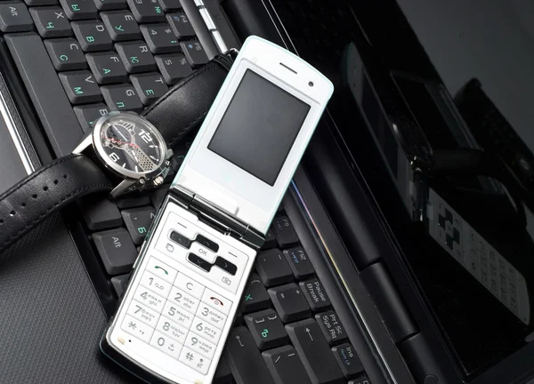 Mobile phone and watch on a laptop — Stock Photo, Image