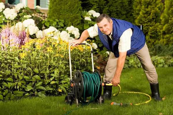 压接软管在花园里的男人 — 图库照片