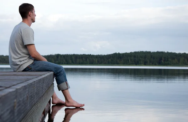 Młody mężczyzna siedzący samotnie przez wodę — Zdjęcie stockowe
