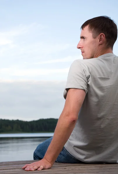 Um jovem sentado sozinho junto à água — Fotografia de Stock