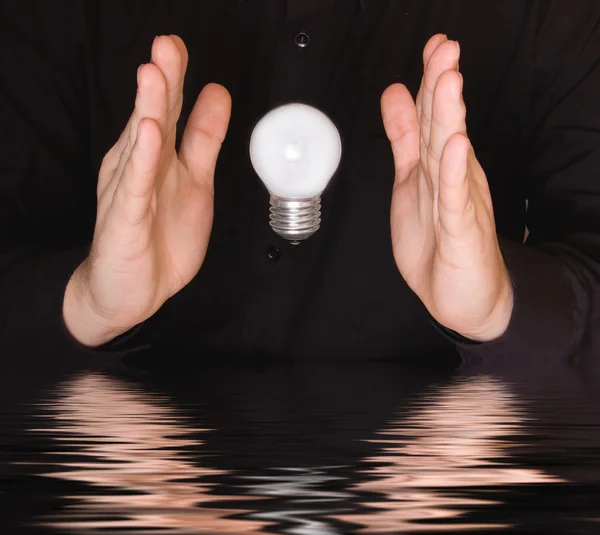 stock image Flying electrical bulb between palms