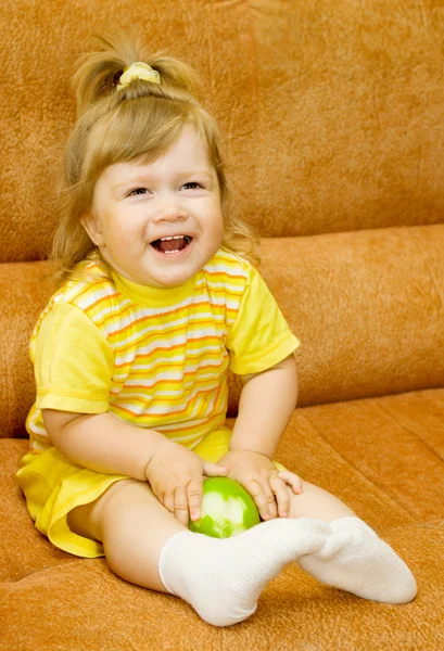 Маленькая улыбающаяся девочка в желтом ест яблоко — стоковое фото