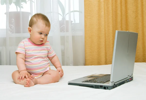 Маленький ребенок и ноутбук на кровати — стоковое фото