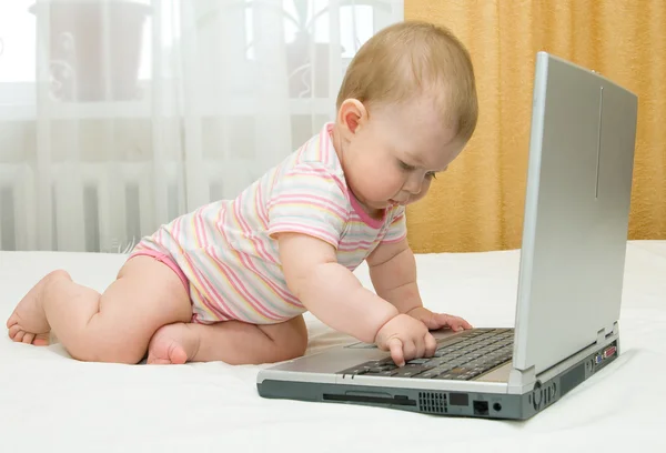 Pequeno bebê e laptop na cama — Fotografia de Stock