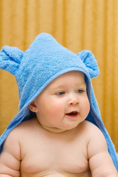 Маленький улыбающийся ребенок в синем полотенце на кровати — стоковое фото