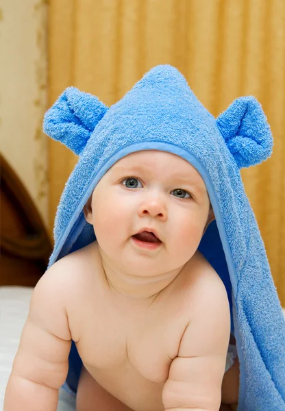 Улыбающийся ребенок в синем полотенце на кровати — стоковое фото
