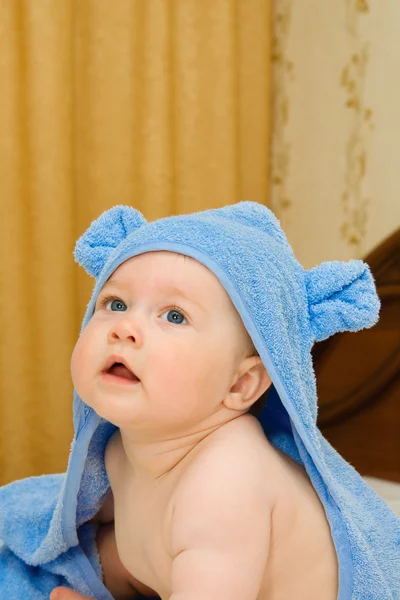 Улыбающийся ребенок в синем полотенце на кровати — стоковое фото