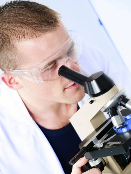 Hombre sonriente investigando en un microscopio —  Fotos de Stock