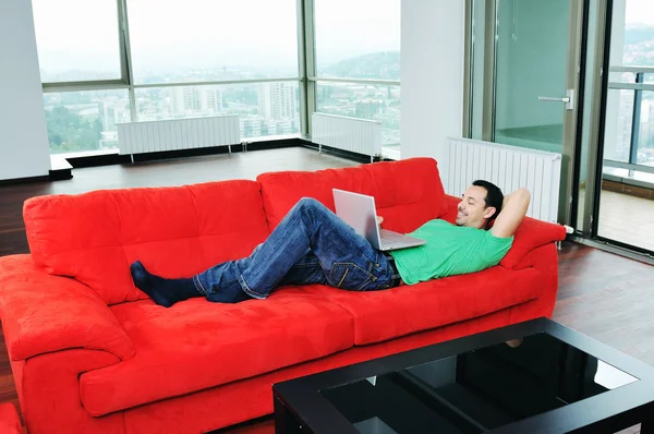 Άνθρωπος να χαλαρώσετε στον καναπέ και να εργάζονται στο lap-top幸せなカップルの赤いソファでリラックスします。 — Φωτογραφία Αρχείου