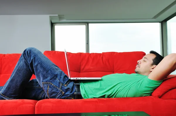 Άνθρωπος να χαλαρώσετε στον καναπέ και να εργάζονται στο lap-top幸せなカップルの赤いソファでリラックスします。 — Φωτογραφία Αρχείου
