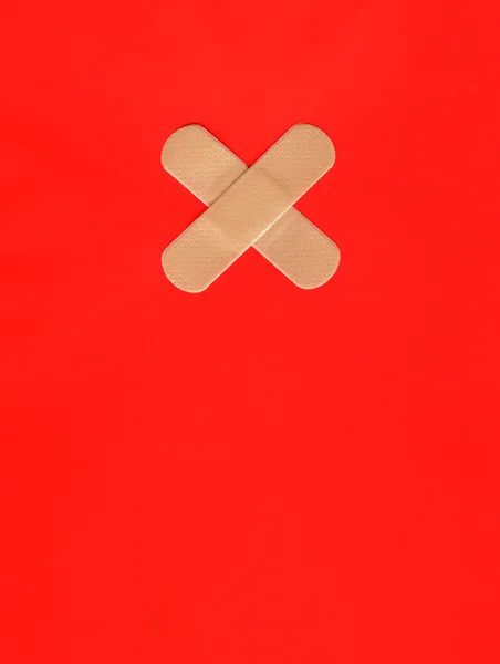 Twee pleisters vormen een kruis op rood — Stockfoto