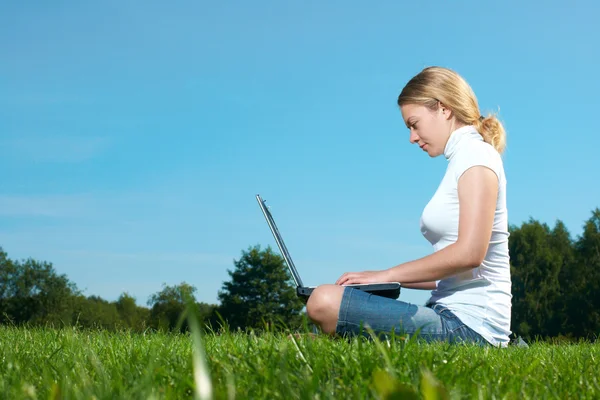 La ragazza con computer portatile su un prato verde — Foto Stock