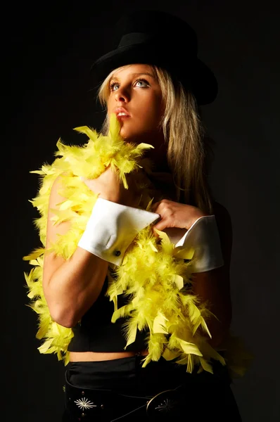 黒の背景に帽子と黄色の羽を着てかなりブロンドの女性 — ストック写真