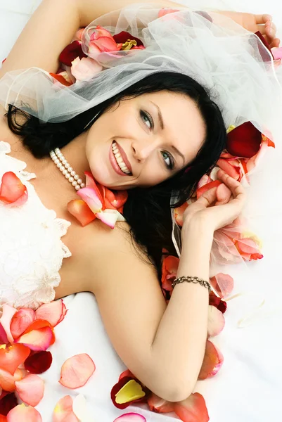 用玫瑰树叶盖在床上的黑发新娘 — 图库照片