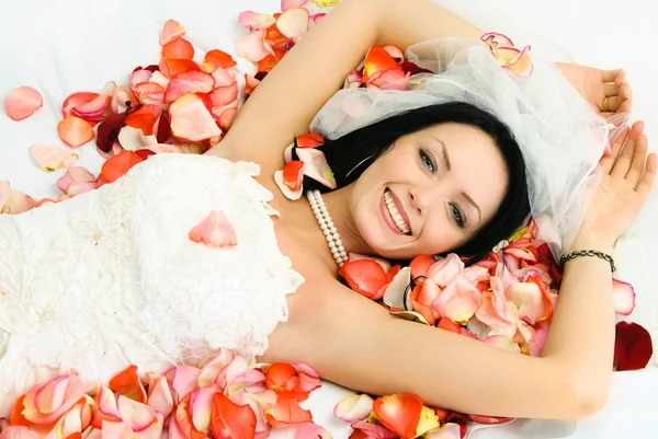 Брюнетка невеста на кровати, покрытой листьями розы — стоковое фото