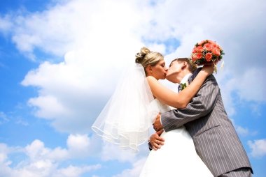 Bride and groom kissing against blue sky clipart