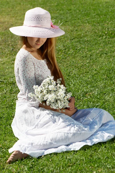Flicka i en hatt med en massa blommor — Stockfoto