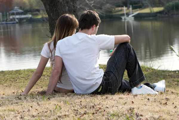 Jovem par sentado na margem do lago — Fotografia de Stock