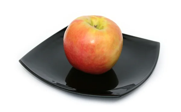 Спелое яблоко на черной тарелке — стоковое фото