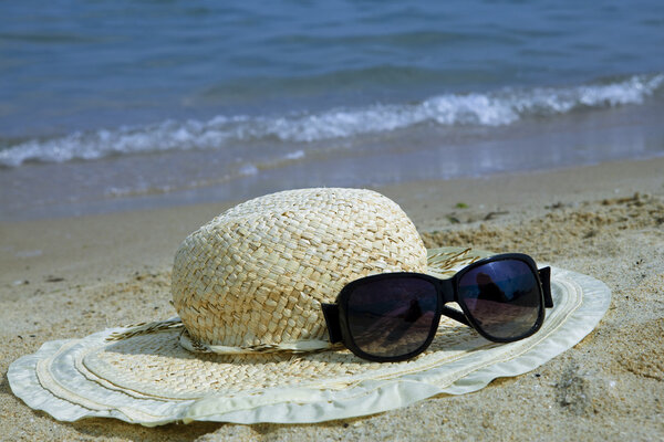 The straw hat and Sunglasses lay on sand at edge of sea