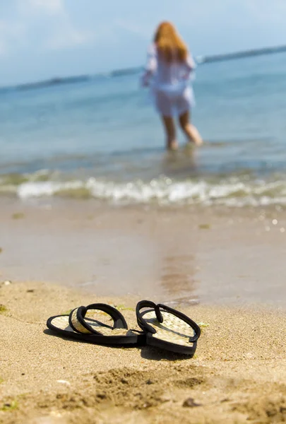 Пляжные тапочки на песке и девушка — стоковое фото