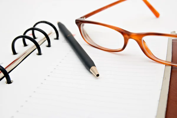 Caderno aberto com caneta e óculos — Fotografia de Stock