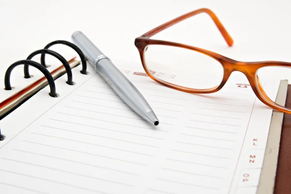 Caderno aberto com caneta e óculos — Fotografia de Stock
