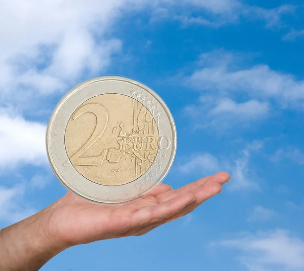 Moeda de dois euros na mão no fundo do céu backgrou — Fotografia de Stock