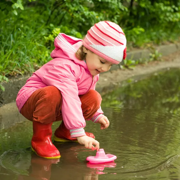 Girl playing with ship in the puddle — Stock Photo, Image