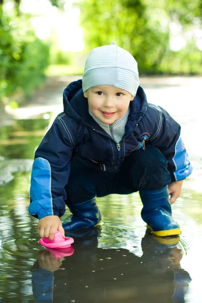 Little boy plays with ship in the puddle — Stock Photo, Image