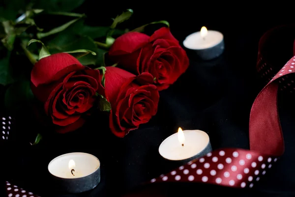 Drie rode rozen en brandende kaarsen — Stockfoto