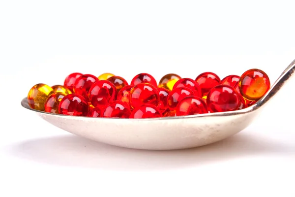 Spoon with red and yellow capsules — Stock Photo, Image