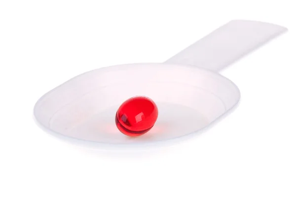 Red capsule on a white plastic spoon — Stock Photo, Image
