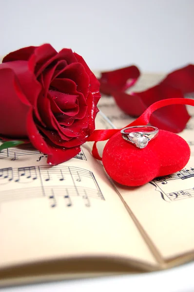 Rosa roja y pétalos en hoja de música con corazón de tela —  Fotos de Stock