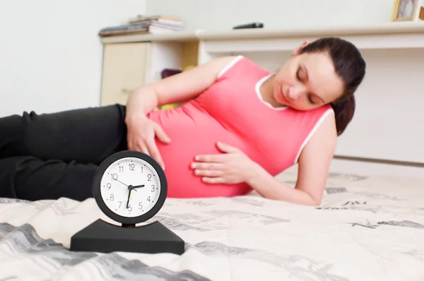 Mujer embarazada mentirosa y reloj —  Fotos de Stock