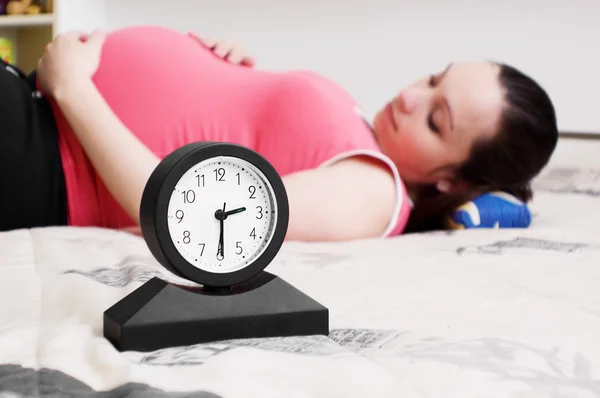 Mujer embarazada mentirosa y reloj Fotos de stock libres de derechos