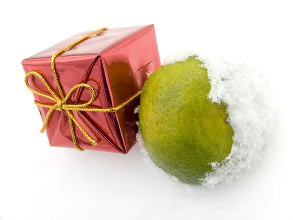 Tangerine and a christmas gift on snow — Stock Photo, Image