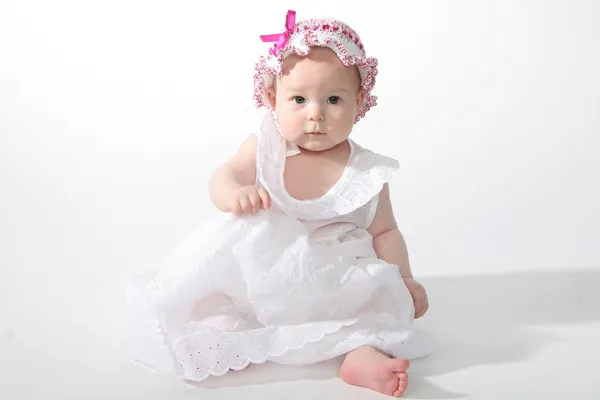 Den lilla flickan i en vit klänning sitter — Stockfoto