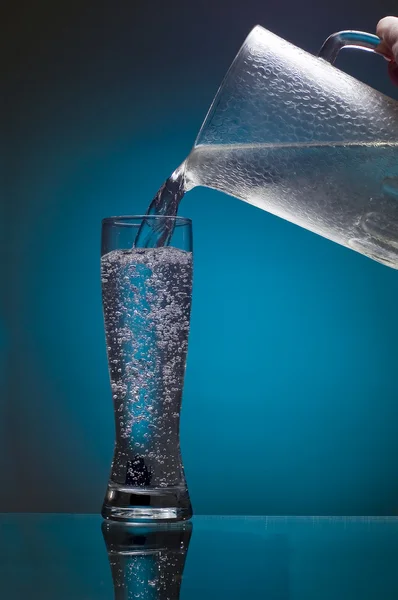 Вода течет из кувшина в стекле — стоковое фото